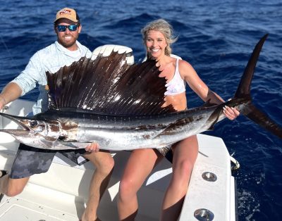 Two friends posing with a beautiful sailfish they caught during a fishing charter in Florida, with the ocean and a blue sky in the background.
