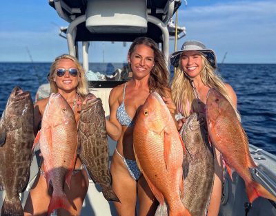 Three women holding up reef fish, including snapper and grouper, during a fishing charter.