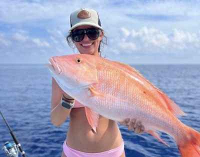 A woman proudly displaying a big mutton snapper caught during a beautiful day fishing charter on the ocean.