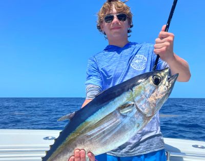 A boy proudly holding a big blackfin tuna caught during a deep-sea fishing charter.