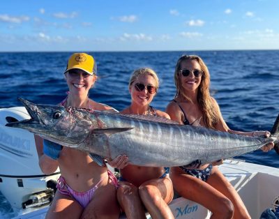 A group of three girls proudly holding a massive 80lb wahoo caught while trolling during a fishing charter