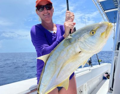 A woman proudly holding a yellow jack fish after a successful fishing charter trip.