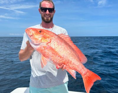 A handsome man proudly holds a red snapper caught during a deep-sea fishing charter.