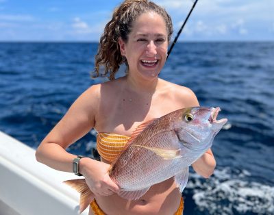 A happy girl showing off a porgy caught on a fishing trip with friends.