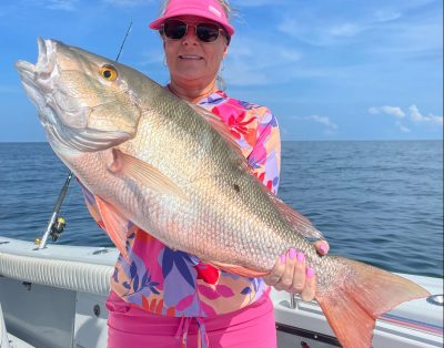 A woman proudly holding a giant mutton snapper caught while fishing key west wreck during a sunny day in Florida.