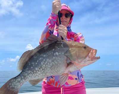 A woman proudly holding a red grouper caught during a sunny day fishing charter in Key West, Florida.
