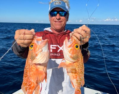 A man proudly holds two rosefish caught while deep dropping on a deep-sea fishing charter.