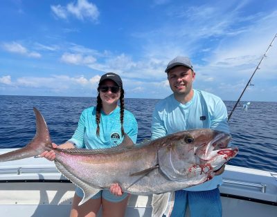 Siblings proudly hold up a massive amberjack fish for the camera during a fishing charter.