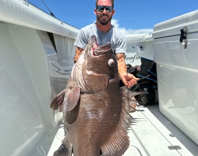 A man proudly holds a 120lb snowy grouper caught during a fishing charter.