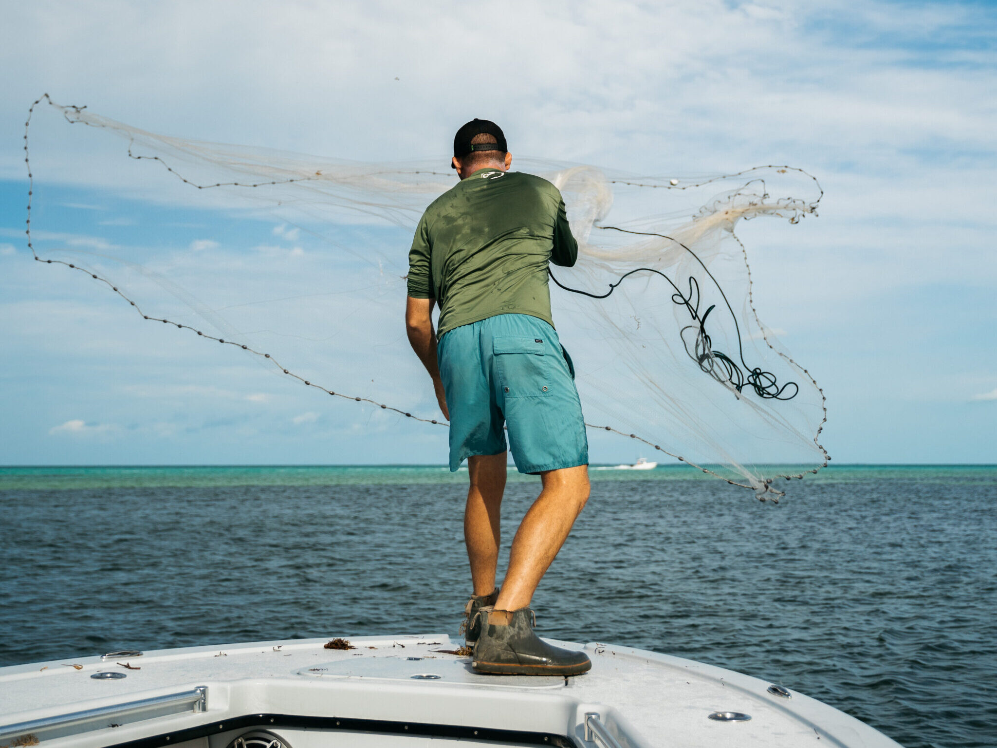 Captain throws bait net in hopes of catching pilchards on a fishing charter in Florida, preparing for an offshore angling adventure.