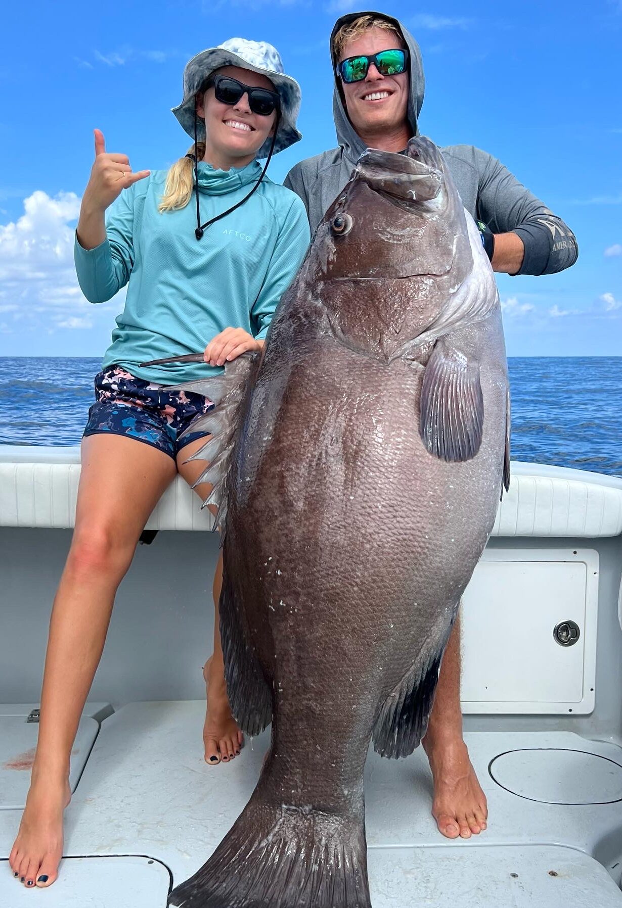 A smiling couple holds up a large grouper caught during a fishing charter off the coast of Florida, showcasing the thrill of deep-sea fishing adventures.