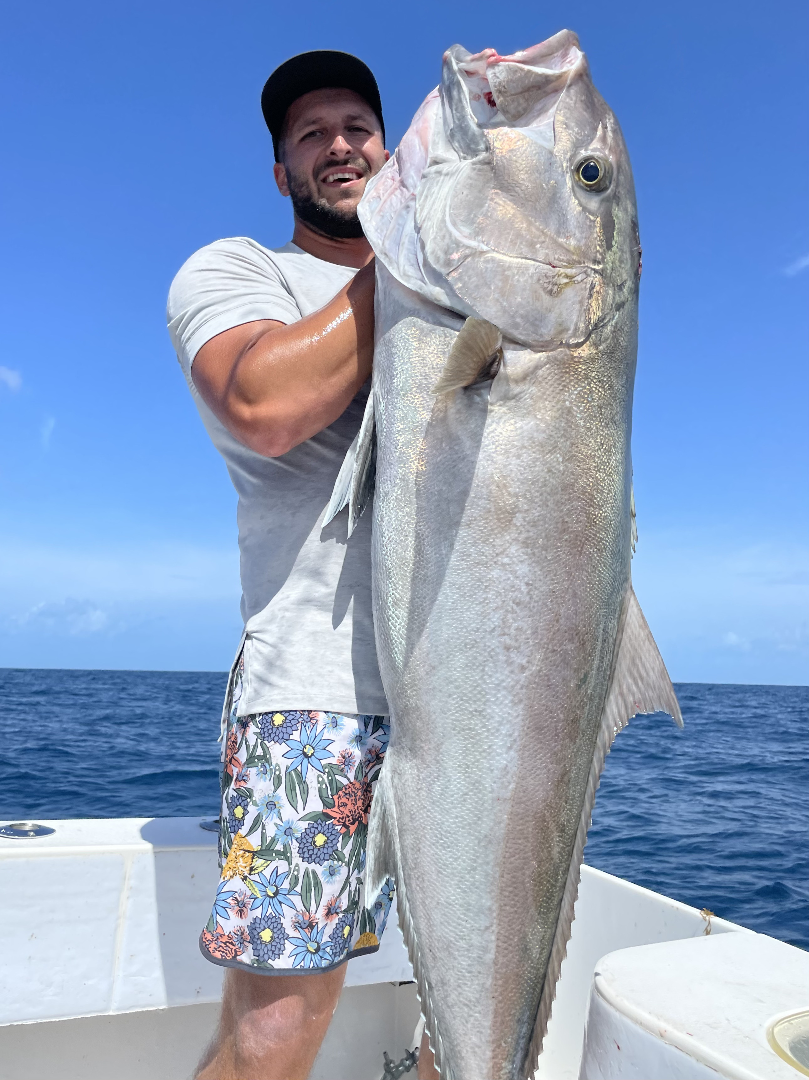 A man holds up a massive amberjack fish caught during a fishing charter, showcasing the impressive size of the catch and the excitement of deep-sea fishing.