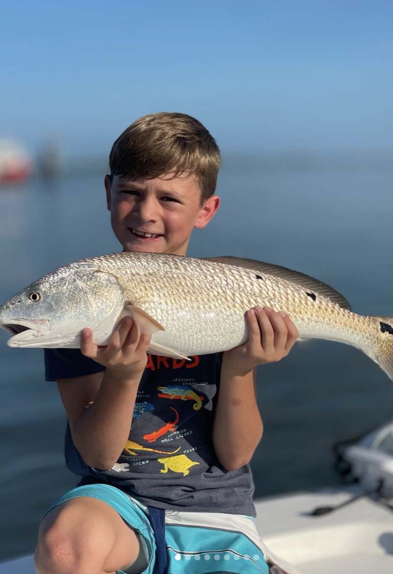 A little boy holds up a a redfish caught during a flats fishing charter off the coast of Florida, capturing the thrill of a successful day of angling in the region's abundant waters.