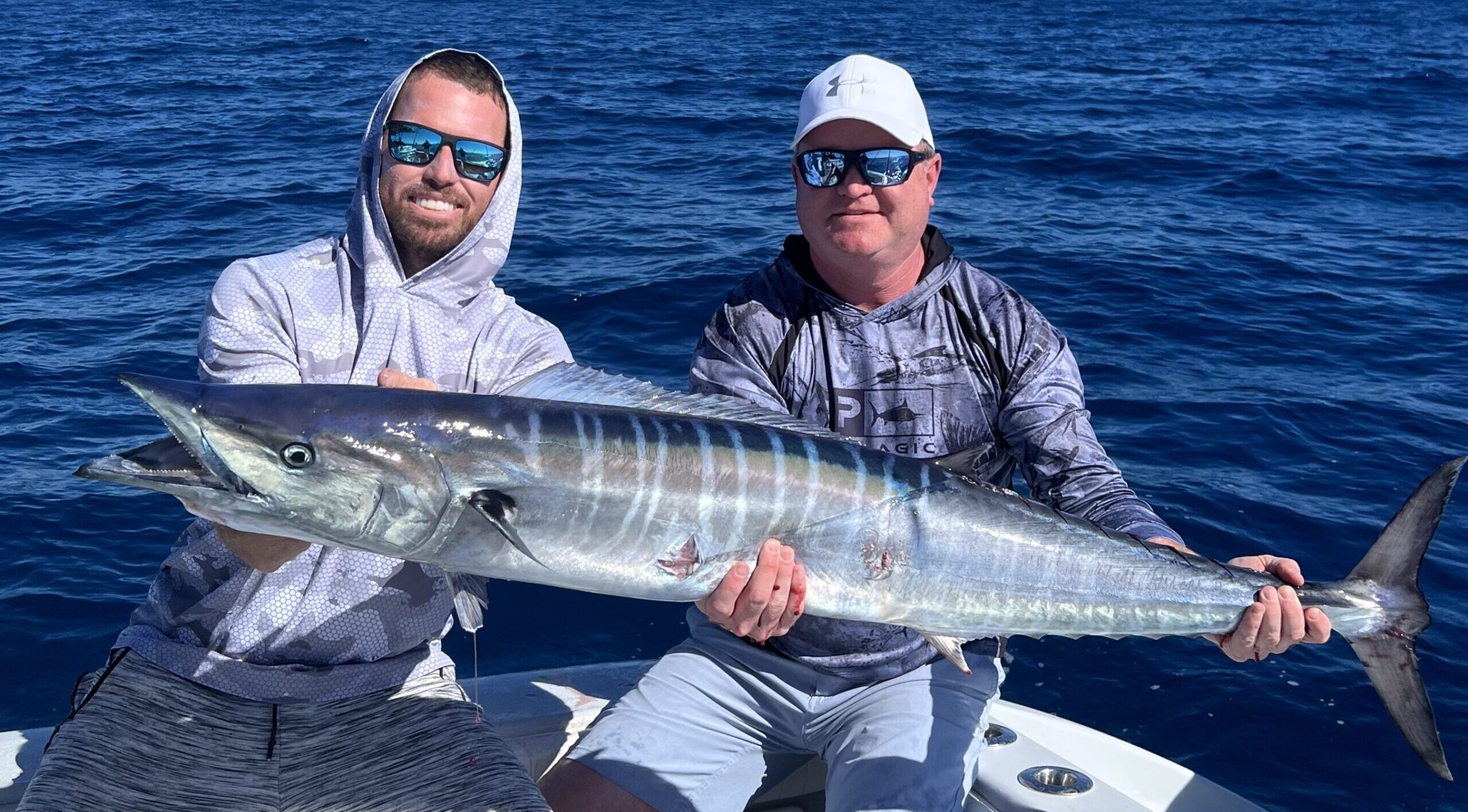 Two anglers proudly showcasing their impressive catch during a successful wahoo fishing charter.