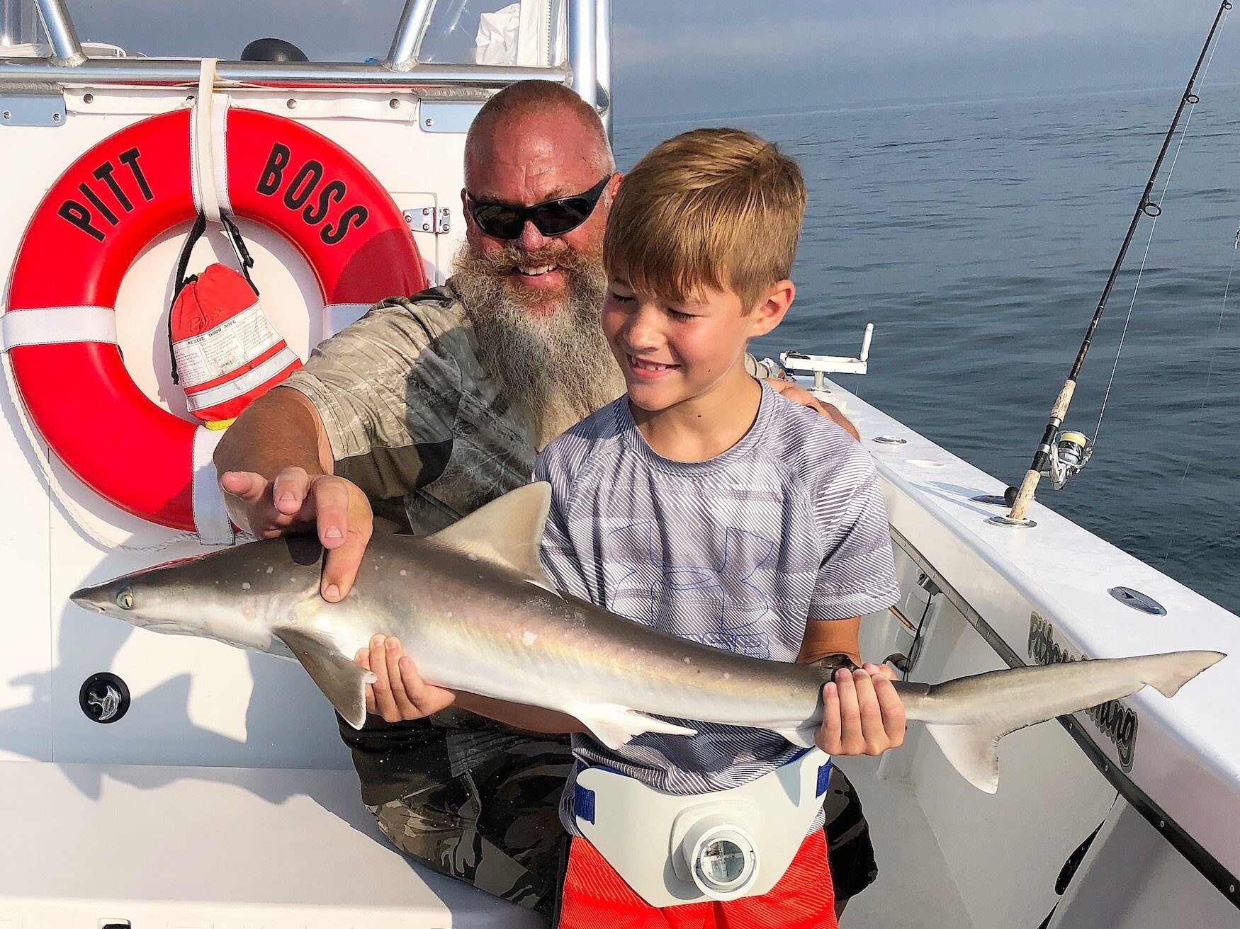 Small boy and father holding up small shark while on shark fishing charter in Miami, Florida before releasing back into the ocean.