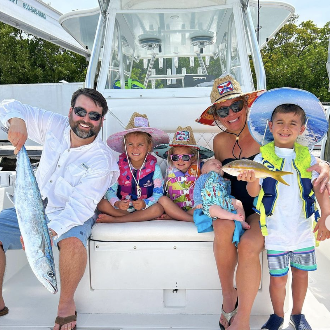 Image of a family of five sitting on a fishing charter boat, enjoying a family-friendly fishing trip together. The background features the calm waters and scenic views, highlighting the bonding experience of fishing as a family.