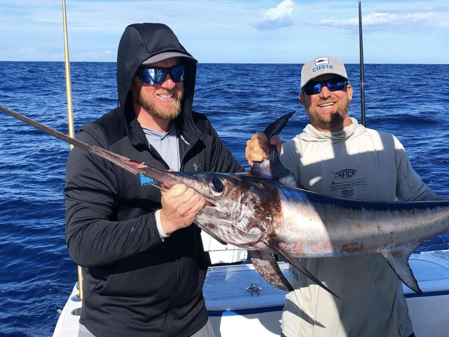 Two friends on a swordfish fishing charter in Florida, proudly holding their catch with the ocean as a stunning backdrop, highlighting the exhilarating experience of a successful fishing trip.