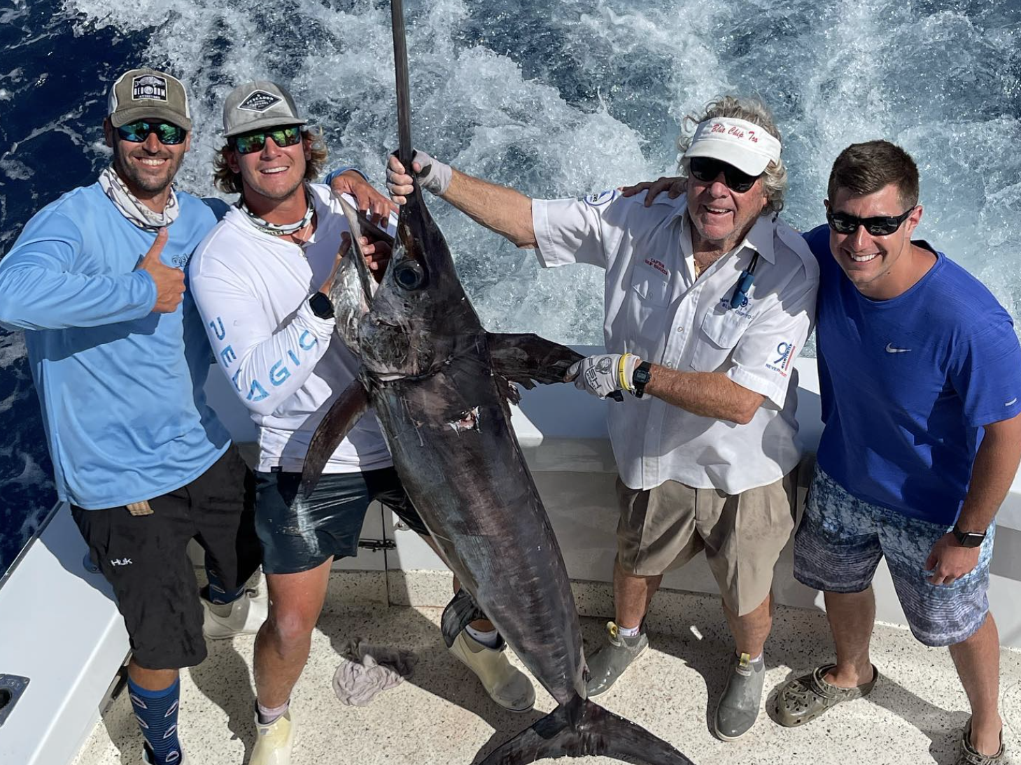 Group of four guys holding swordfish after a successful swordfish charter in Fort Lauderdale, Florida, with the sun and ocean in the background, capturing the excitement and achievement of their fishing adventure.