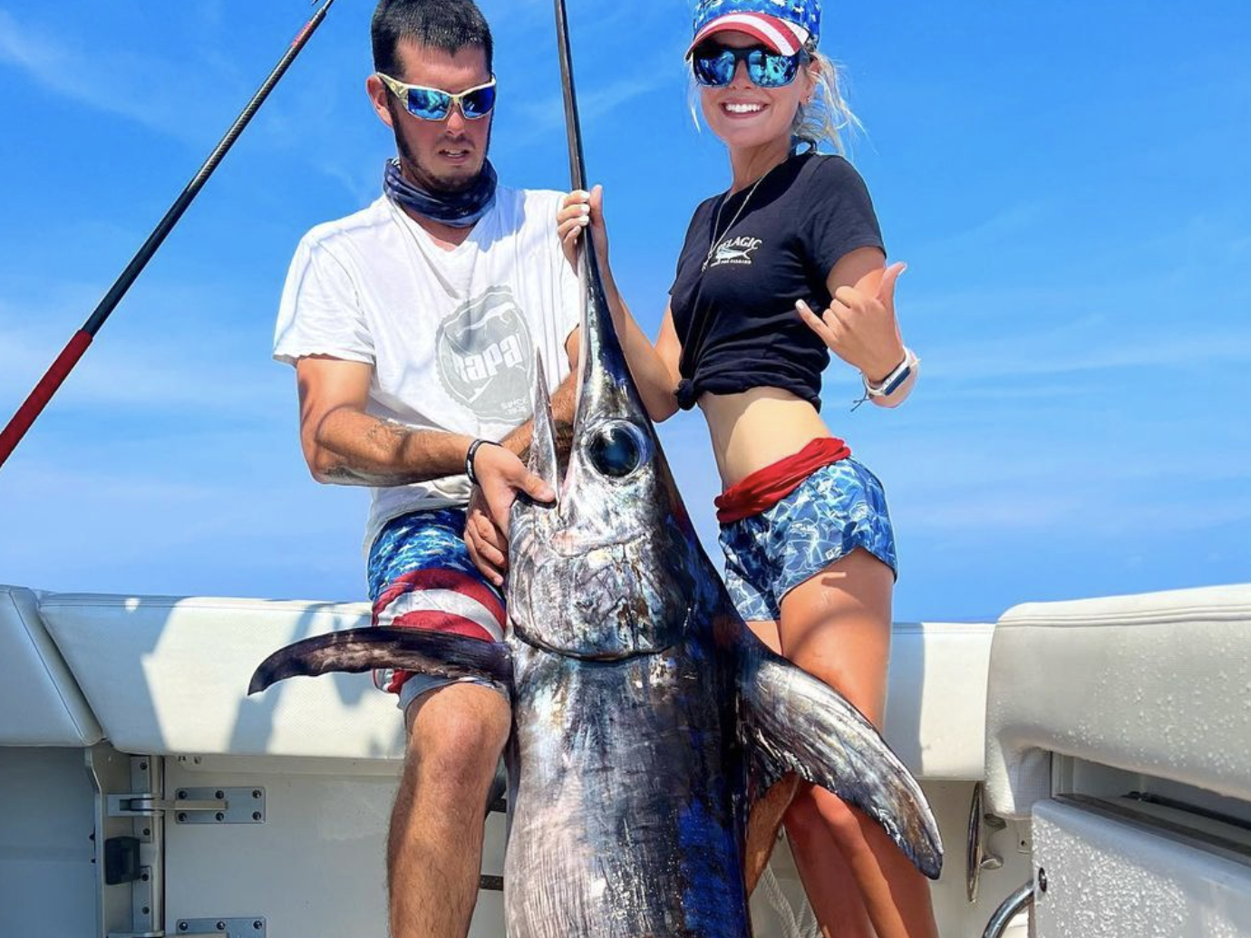 A couple proudly displaying a 350 lb swordfish they caught during a swordfish fishing charter, highlighting their successful and thrilling fishing experience.