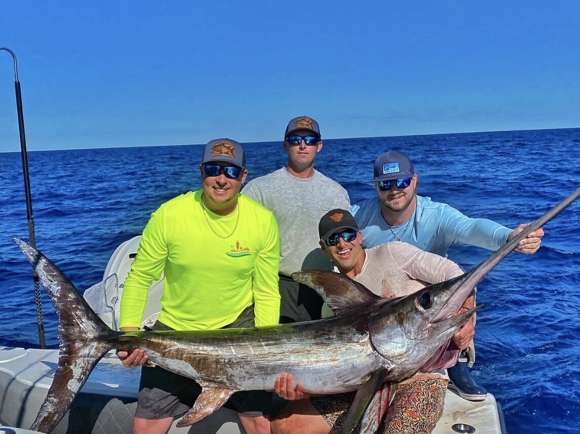 Four friends proudly holding a swordfish they caught while on a fishing charter in Florida, capturing the excitement and camaraderie of a successful fishing trip.