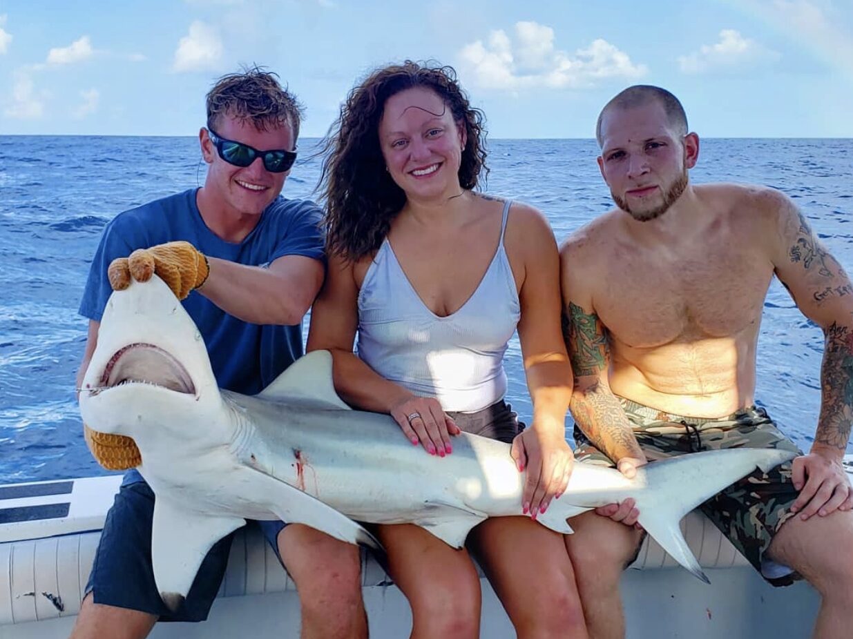 Three siblings hold up a medium-sized shark while on a fishing charter in Florida, with the ocean in the background.