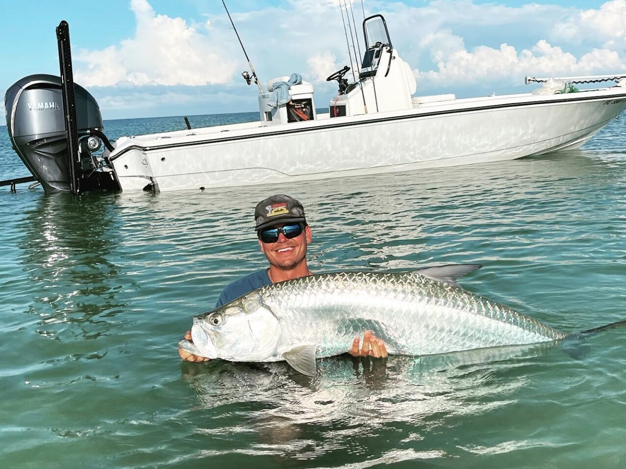 Client holds tarpon in the water during a tarpon fishing charter in Naples, enjoying a beautiful sunny day with the ocean as a backdrop.