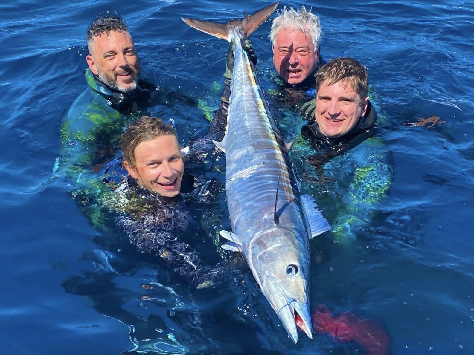 Four men in wetsuits spearfish wahoo fish in the Florida Keys during a spearfishing charter.
