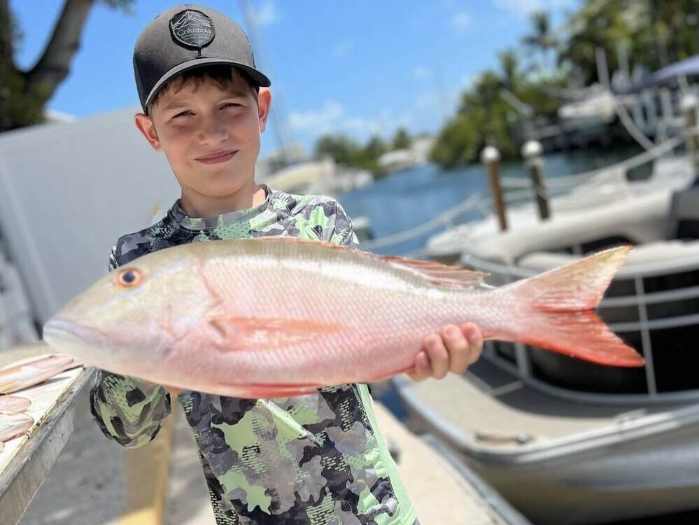 Young boy holding a Mutton Snapper caught during a fishing charter in the Florida Keys, surrounded by family.