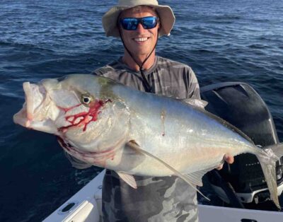 A man proudly posing with a yellow jack he caught during a fishing charter in Florida, with the ocean and a blue sky in the background.