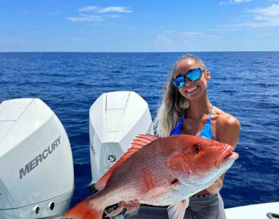 Young woman holding up red snapper, while on a fishing charter in Florida.