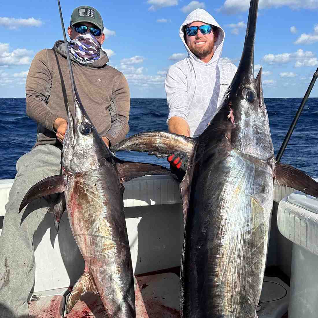 Two friends holding up big swordfish while on fishing charter in Fort Lauderdale.