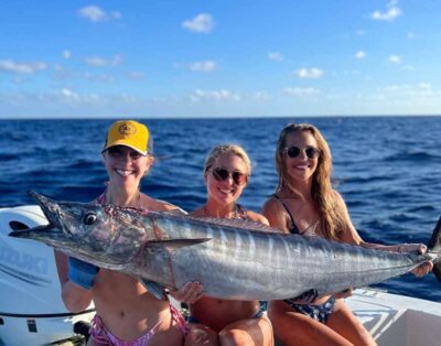 A group of three girls proudly holding a massive 80lb wahoo caught while trolling during a fishing charter