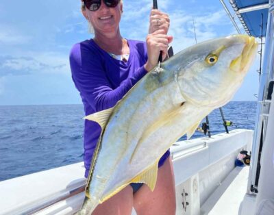 A woman proudly holding a yellow jack fish after a successful fishing charter trip.