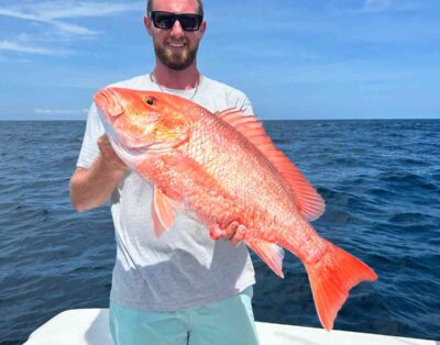 A handsome man proudly holds a red snapper caught during a deep-sea fishing charter.