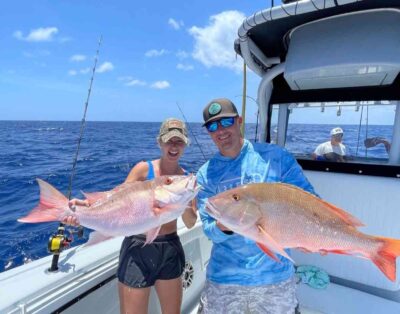 Two people proudly holding up two mutton snappers caught during the mutton spawn while on a fishing charter.