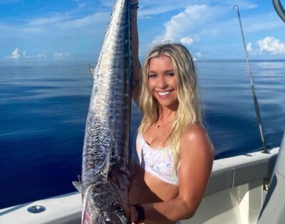 A girl holding up a wahoo fish while on an offshore fishing charter.