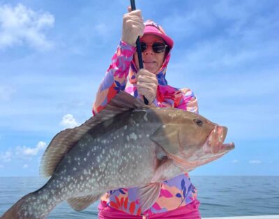 A woman proudly holding a red grouper caught during a sunny day fishing charter in Key West, Florida.