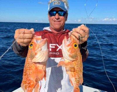 A man holding two rosefish caught while deep dropping on a deep-sea fishing charter.