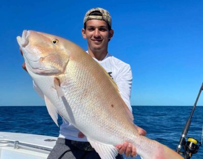 A man proudly displaying a giant mutton snapper caught while on a fishing charter on the ocean.