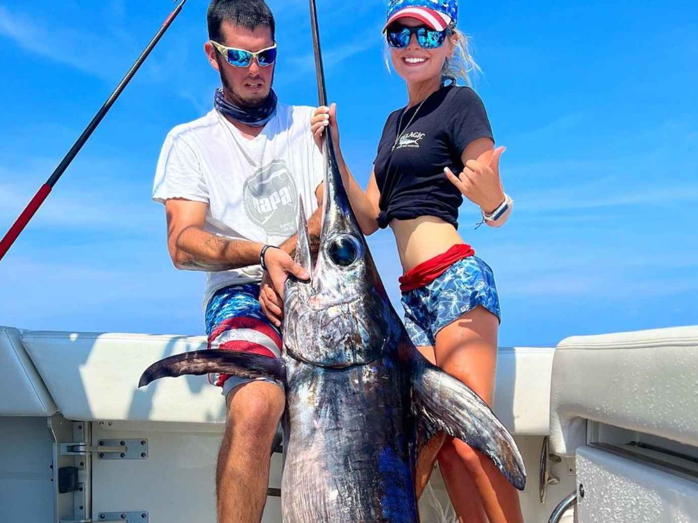 A couple proudly displaying a 350 lb fish they caught during a swordfishing charter, highlighting their successful and thrilling fishing experience.