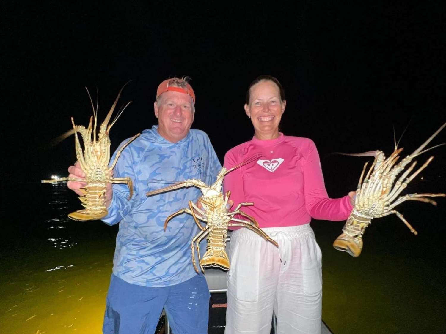 Two happy customers holding up lobster during a night time lobster fishing trip in Key West Florida.