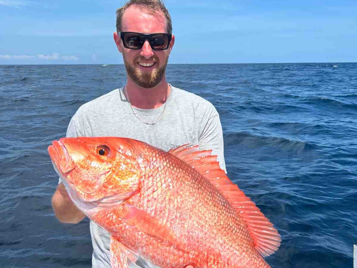 florida keys red snapper male angler smiling Reel Guides Male angler showing off a Florida Keys red snapper caught on an offshore fishing charter.