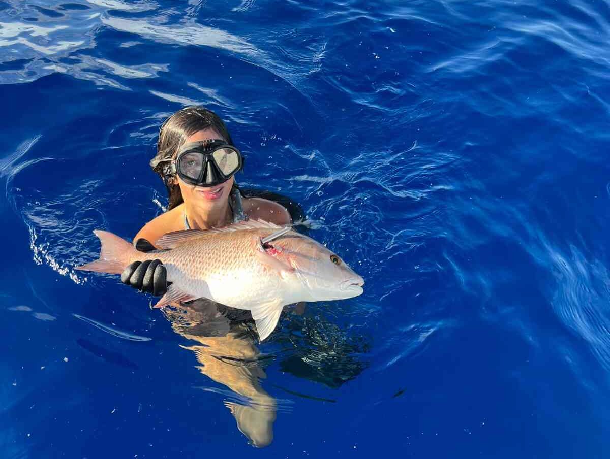 spearfishing girl snapper fish e1758818105874 Reel Guides Woman holding a freshly caught snapper while spearfishing, in the water with the ocean in the background.